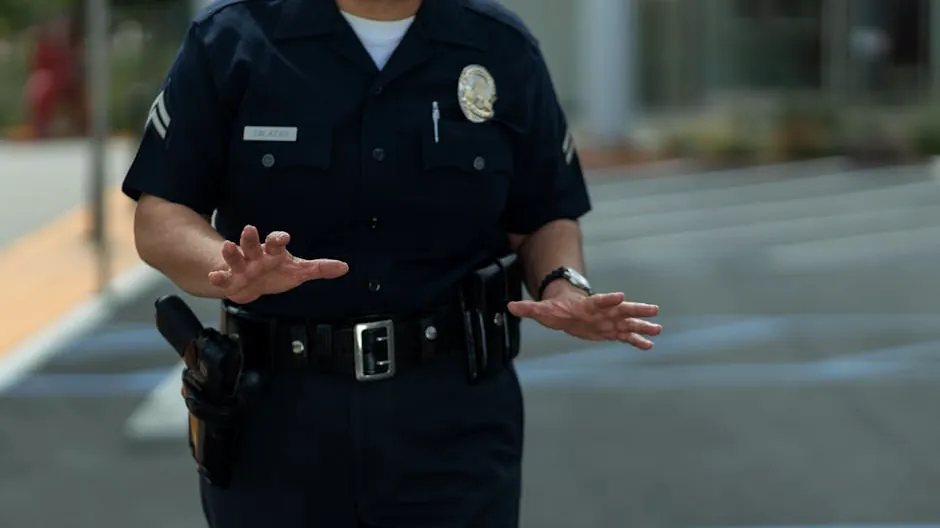 A police officer in uniform making gestures outdoors in a parking lot.