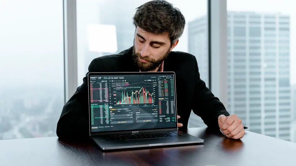Focused trader examines stock market graphs on laptop in office setting.