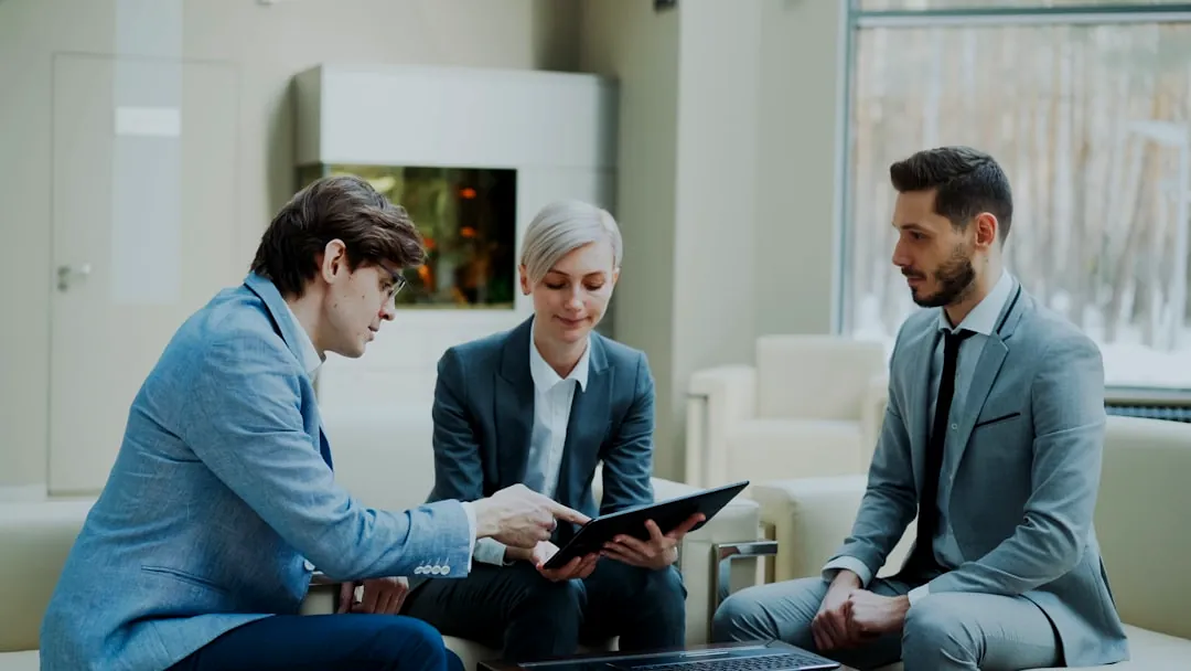 Three professionals discussing a tablet in a modern office.