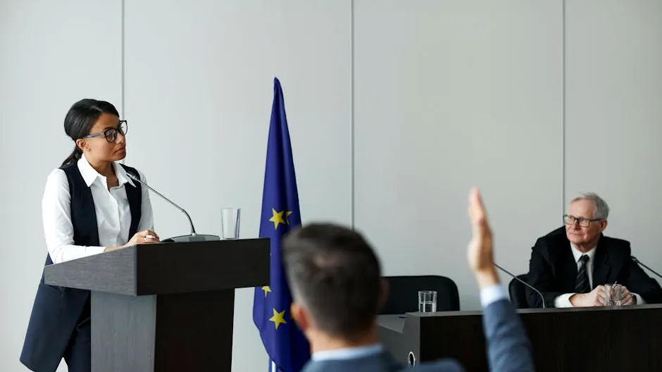 A woman speaking at a European Union conference while delegates listen attentively.